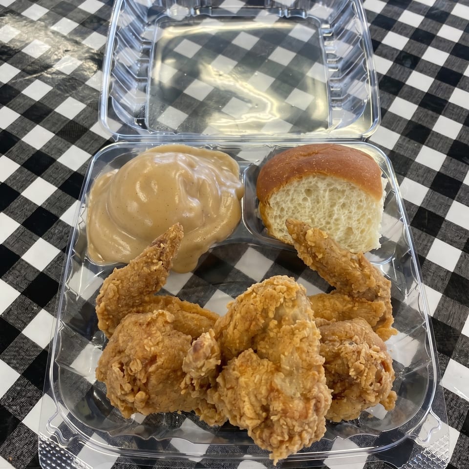 Fried chicken, mashed potatoes with gravy, and a dinner roll in a plastic takeout container.