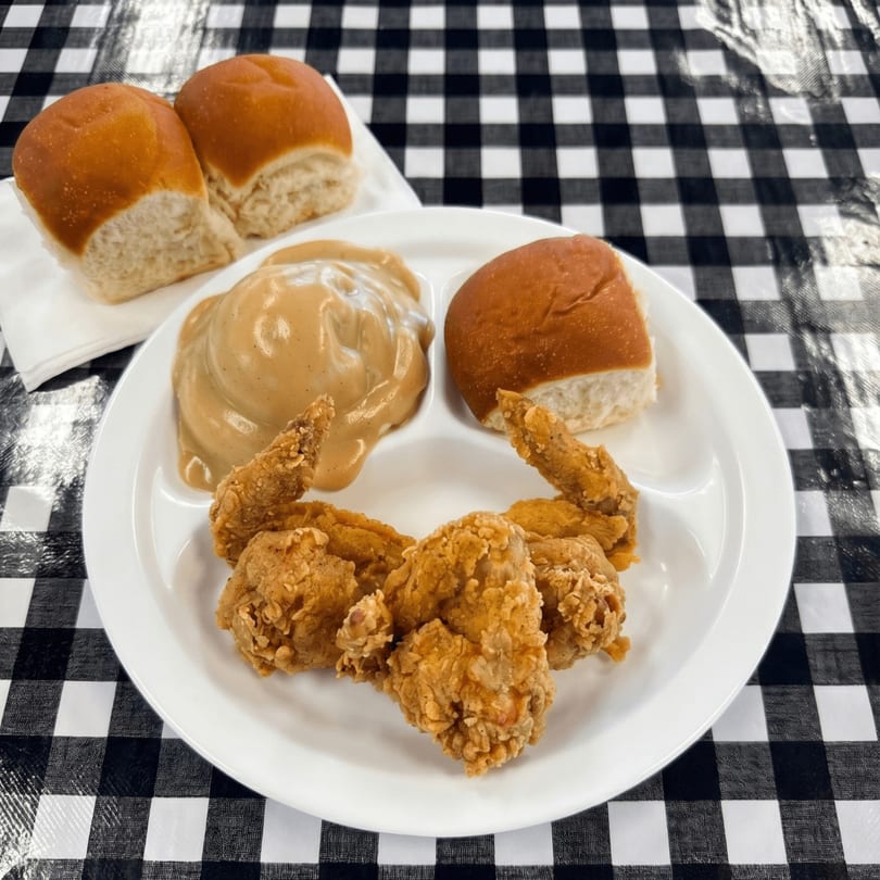Fried chicken wings, mashed potatoes with gravy, and dinner rolls on a white plate.