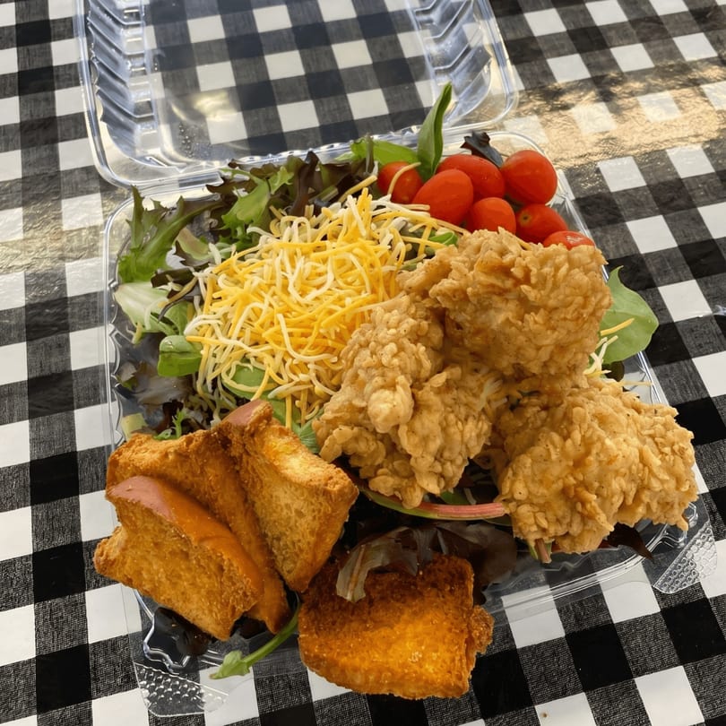 Fried chicken, salad with shredded cheese and cherry tomatoes, and toast in a plastic takeout container.