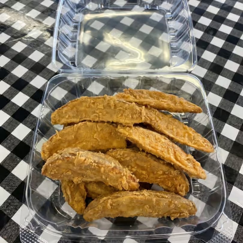 Golden-brown potato wedges in a clear plastic takeout container on a black and white checkered tablecloth.