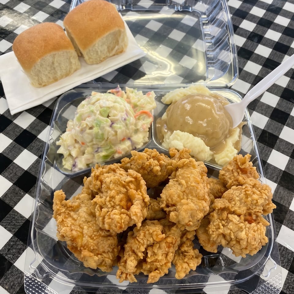 Fried chicken tenders, mashed potatoes with gravy, coleslaw, and dinner rolls in a takeout container.