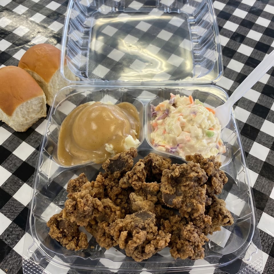 Fried chicken livers, mashed potatoes with gravy, coleslaw, and dinner rolls in a takeout container.